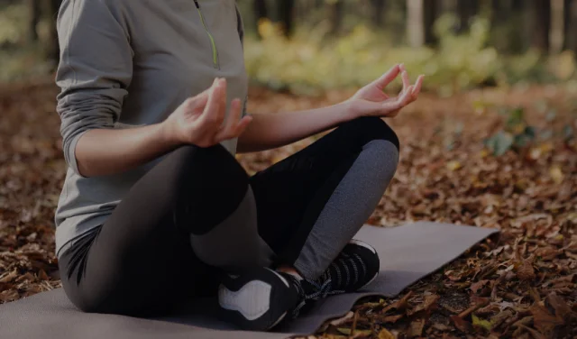 Crossed legs and resting hands of a student seated on a yoga mat