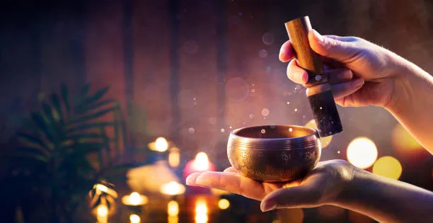 Hands holding a singing bowl over warm candlelight